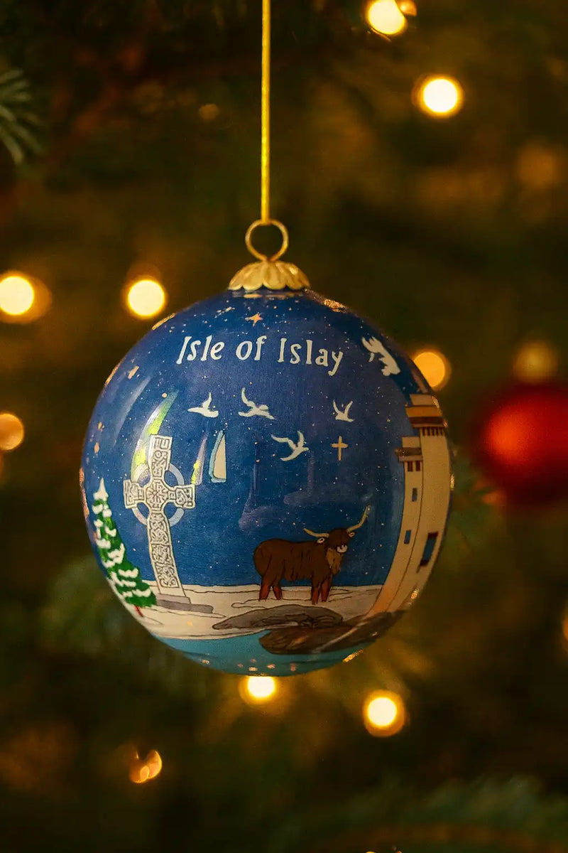Blue Christmas ornament with ’Isle of Islay’ written on it and a depiction of a Highland cow, a Celtic cross, and a lighthouse.
