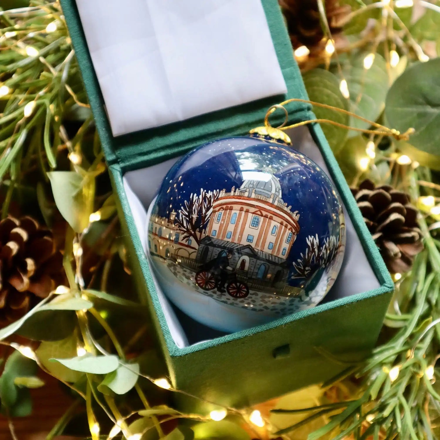 A dark blue Christmas ornament with a hand-painted winter scene, featuring a domed building and a horse-drawn carriage.